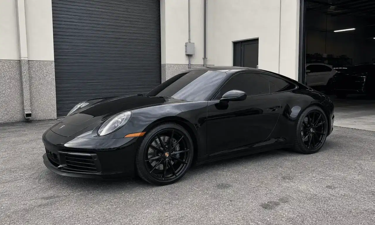 Black Porsche 911 with dark tinted windows outside a tint workshop