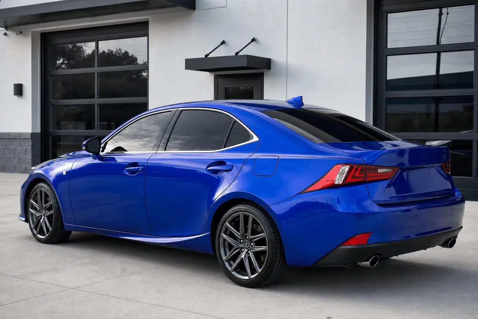 Blue Lexus IS-style sport sedan with dark reflective window tint outside a clean tint workshop